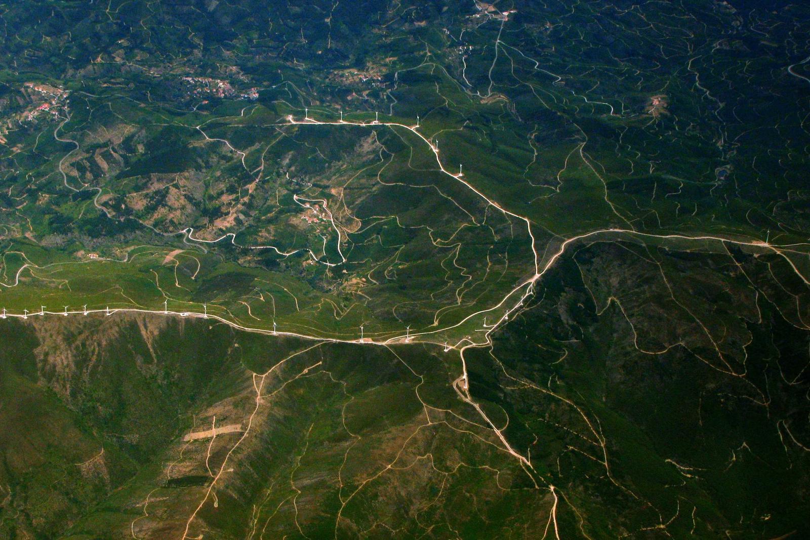 Aerial view of green hills crossed by gravel roads and a line of wind turbines