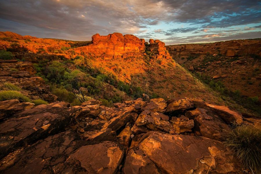 Layered orange rock outcrop in low sun with a sloped face behind