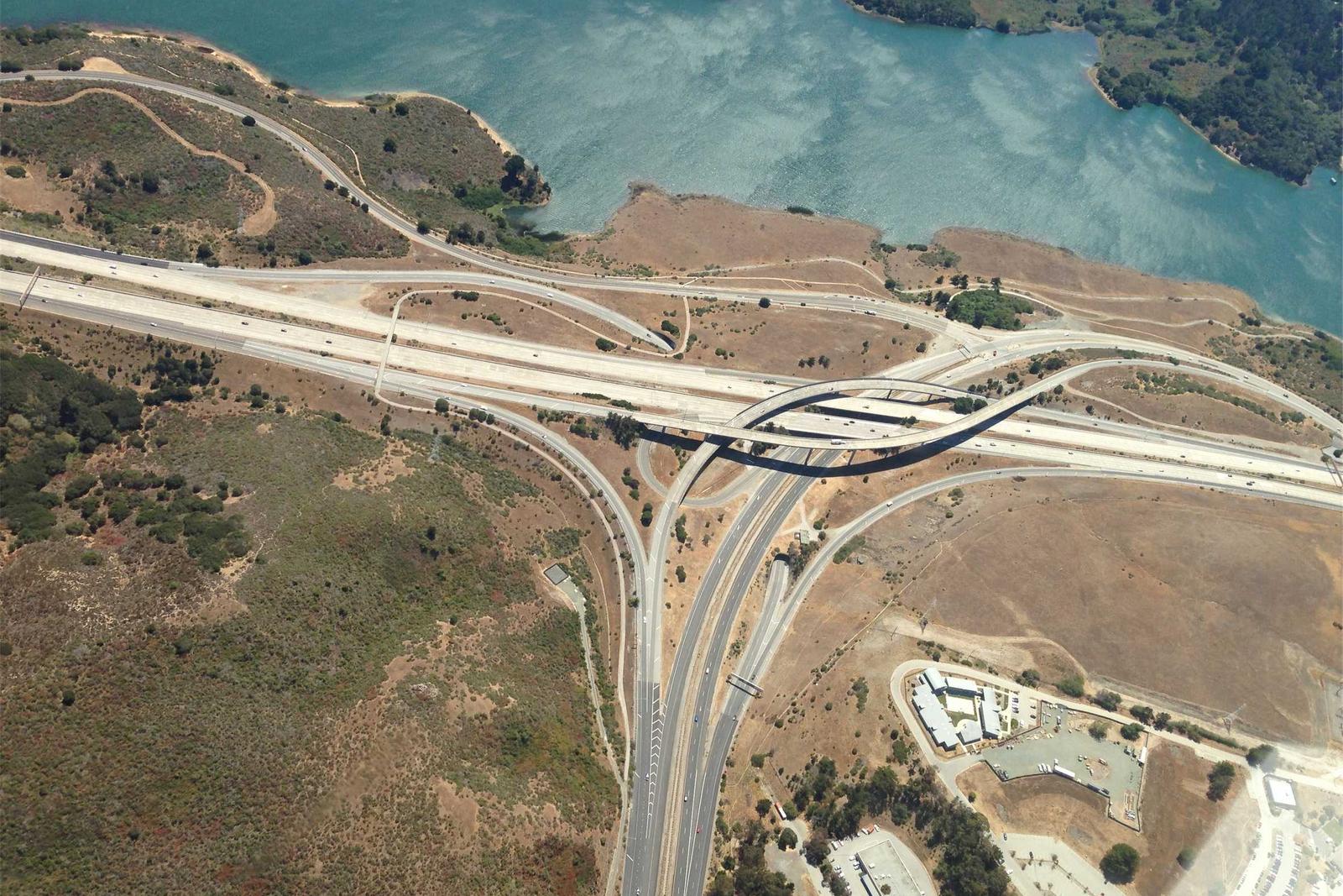 Aerial view of a highway interchange with ramps and overpasses beside a reservoir