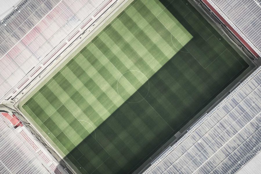 Overhead view of a striped grass playing field inside a stadium, half in shadow